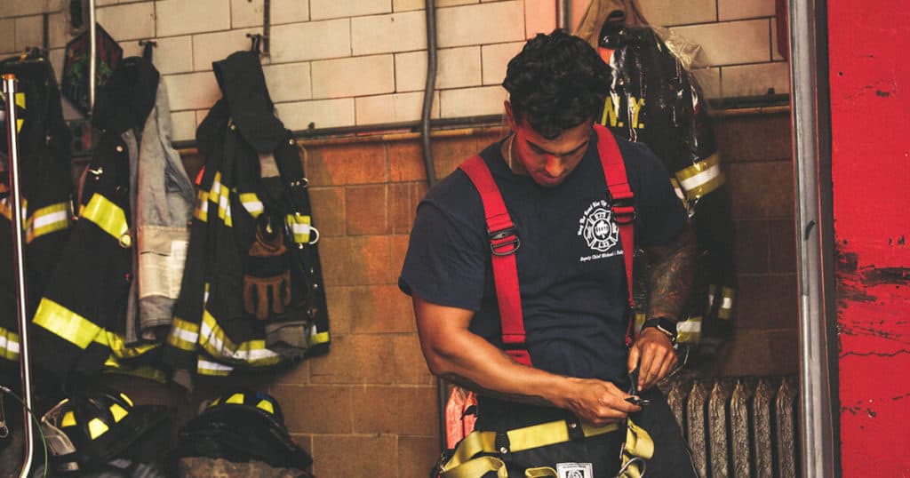Firefighter adjusting his duty belt in the fire station. Looking down and thinking about missing his family on Christmas Day. | YTherapy blog on “First Responders and Family – Surviving Christmas and Beyond” for London First Responders