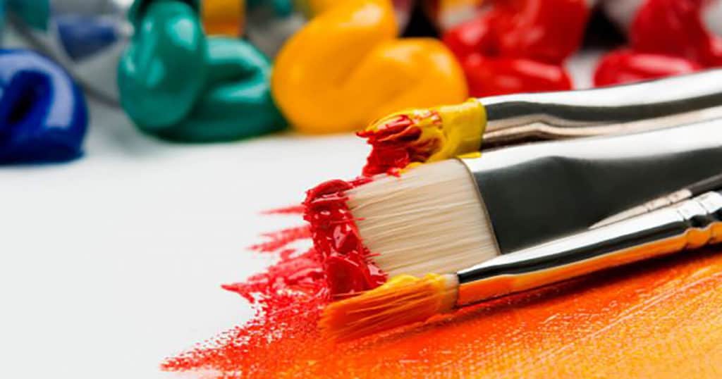 A set of paintbrushes dipped in multi-coloured paints on canvas