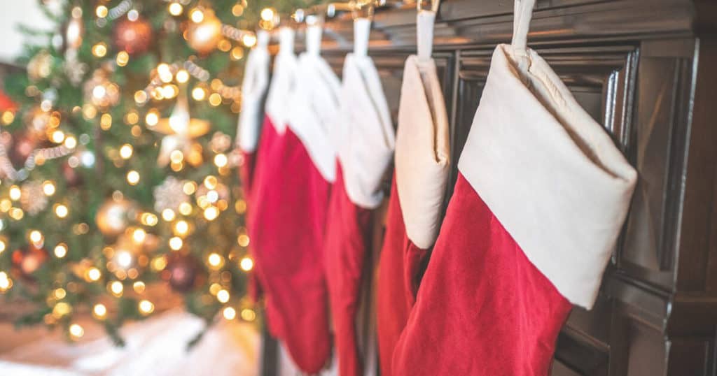 Red and white Christmas stockings are seen hanging in a row with a lit up Christmas tree behind. Preparing for Christmas can be stressful, especially for workaholics, yet stress can be successfully managed with good self-care and stress and burnout therapy in Central London.