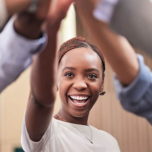 Young professional woman standing in a circle with co-workers giving a high five. At YTherapy, workplace wellness helps build positive relationships and healthy work cultures.
