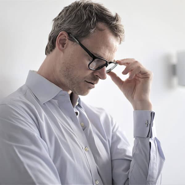 Man with eyes closed adjusts his glasses. Working in the City of London, this lawyer experiences anxiety and panic attacks. With help from his law firm, the lawyer can access counselling with YTherapy.