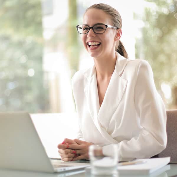 Professional woman with glasses wearing a white blouse is smiling at her clients. As a family lawyer, she takes care of her mental health through YTherapy's workplace wellness programme.