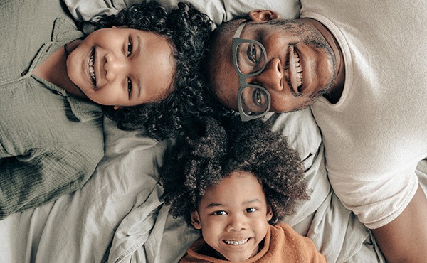 Smiling father and two children are lying down with heads together. Through therapy, this man re-discovers his confidence and can better cope with daily stresses of family life.