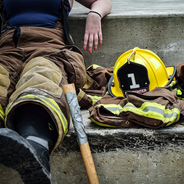 Female firefighter sits on steps after a day's work. This first responder is exhausted and on the brink of burnout due to the demands of work in emergency services.