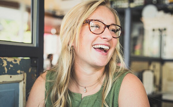 Professional woman wearing glasses smiles with confidence. Through therapy, this London professional feels less stressed and more balanced at work and in life.