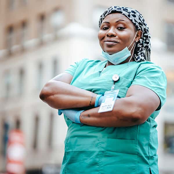 Senior nurse stands confidently in the streets of London with a smile and arms crossed. As a specialist nurse working in oncology and palliative care, she also takes good care of her own mental health and wellness.