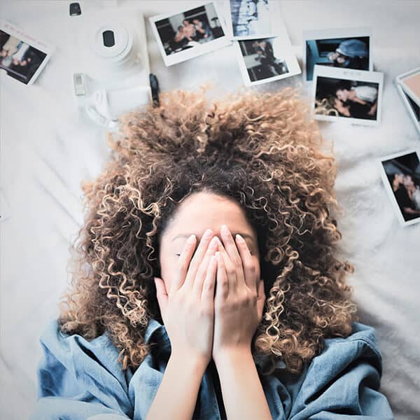 Woman with hands covering her face. The woman is surrounded by polaroid pictures symbolic of trauma memories and PTSD flashbacks.
