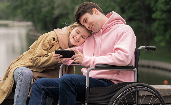 Smiling woman cuddles man in wheelchair. Through trauma therapy, the man can better cope with the pain and loss of his mobililty since recovering from a traumatic car accident.
