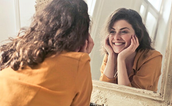 Confident and happy woman looks at her relflection and smiles in the mirror. Through trauma therapy with YTherapy, this woman is no longer feeling trapped by her childhood trauma.